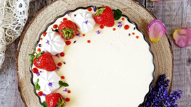 Cream Tea Cheesecake served on a wooden board, topped with strawberries and mini meringues