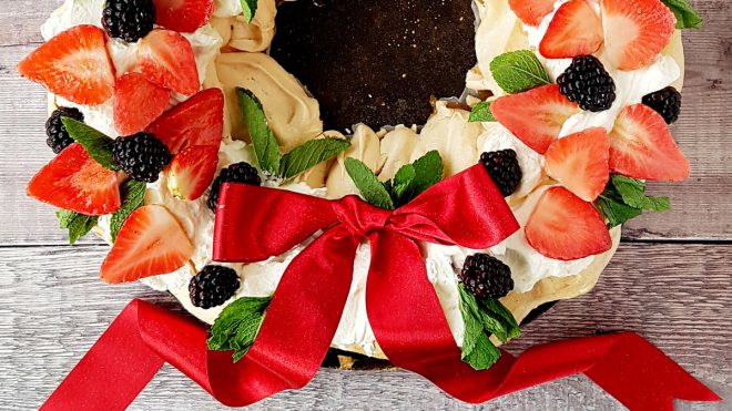 Golden Prosecco Pavlova Wreath served on a wooden board with a red ribbon bow