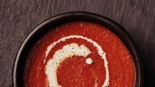 Cream of Tomato Soup served in a dark brown bowl, with a swirl of cream and cracked black pepper