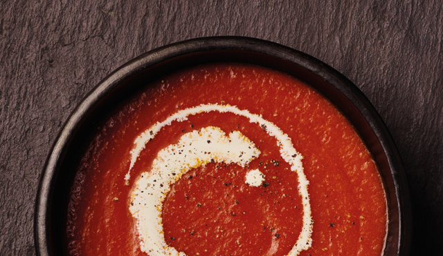 Cream of Tomato Soup served in a dark brown bowl, with a swirl of cream and cracked black pepper