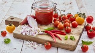 Tomato and Chilli Passata served ina glass jar, surrounded by vine tomatoes, chillies and onions.