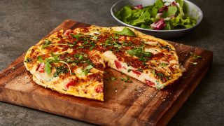 Tomato , Kale and Goats' Cheese Frittata served on a wooden board with a slice removed