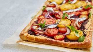 Tomato, Tapenade and Anchovy Tart served on baking parchment and topped with watercress