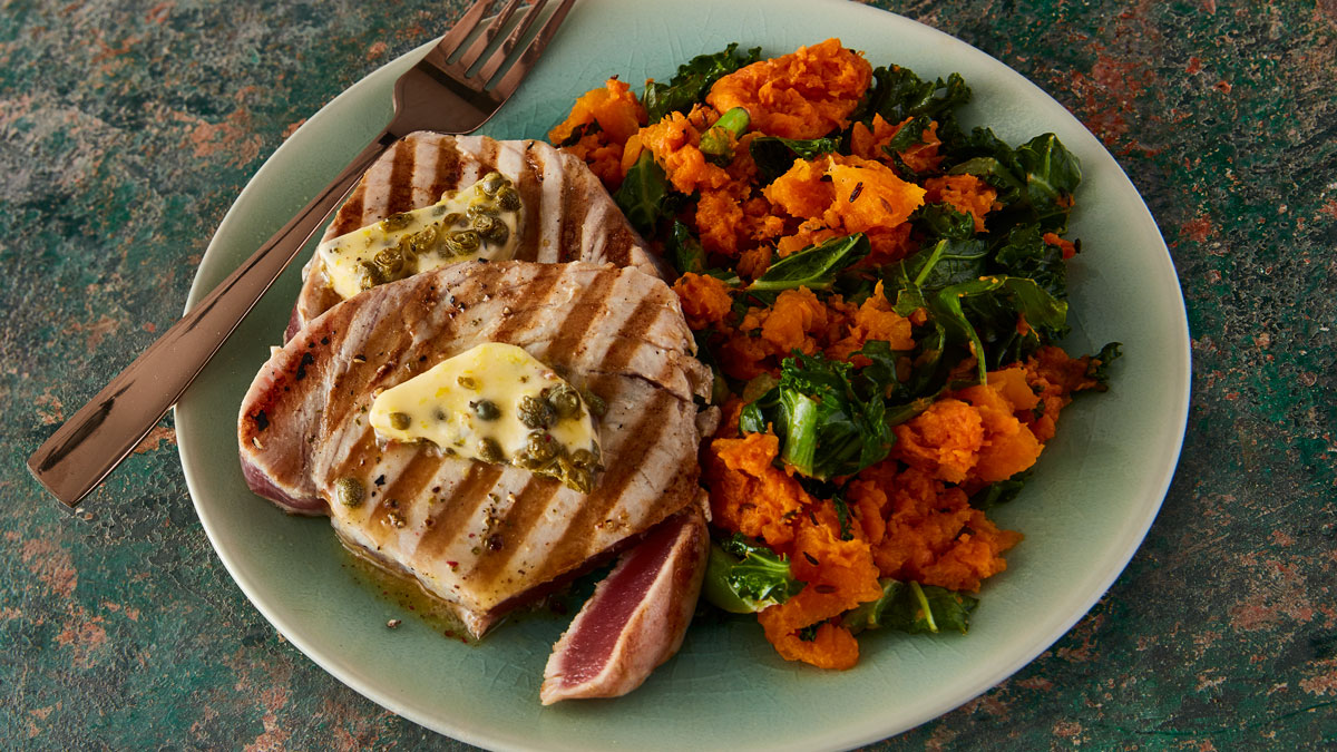 Grilled Tuna Steaks with Lemon Caper Butter and Autumn Mash served on a blue plate