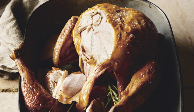 The Perfect Roast Turkey with Chestnut Stuffing served in a baking dish, with some of the turkey carved