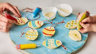 White Chocolate Easter Eggs being decorated with icing pens on a blue wooden board